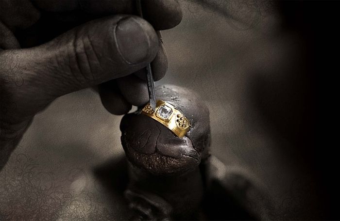 Kunstvolle Nahaufnahme einer Hand, die einen goldenen Siegelring mit einem Diamanten graviert, in dunkler, stimmungsvoller Beleuchtung.